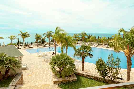 En udendørs pool med omkringliggende liggestole og palmer med udsigt over havet. (AI-genereret tekst)