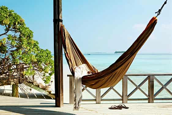 En hængekøje hænger mellem to stolper på en veranda med udsigt over turkis hav. (AI-genereret tekst)