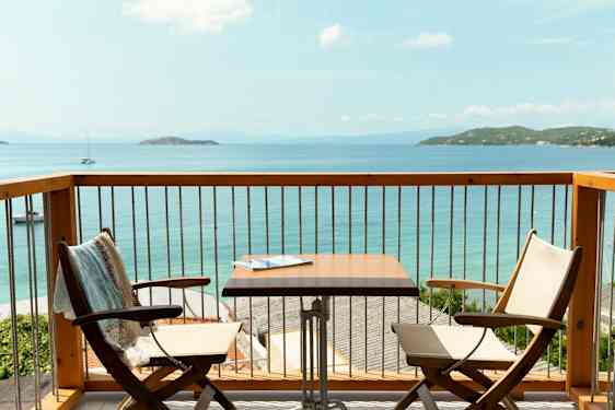 Udsigt fra en altan med to stole, et bord og havet i baggrunden. (AI-genereret tekst)