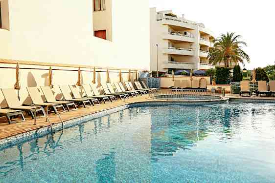 En udendørs swimmingpool omgivet af liggestole og parasoller, med en bygning og en palme i baggrunden. (AI-genereret tekst)