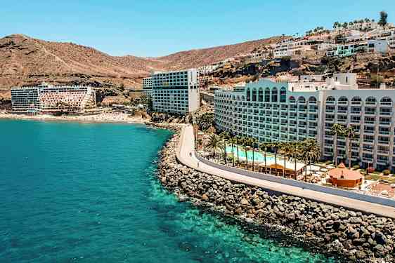 Hotel ved en kyst med klipper, pool og palmer. (AI-genereret tekst)