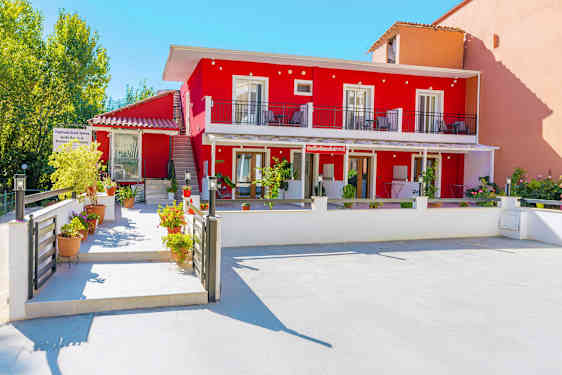 Billede af en rød bygning med altaner og blomsterpotter i forgrunden. (AI-genereret tekst)