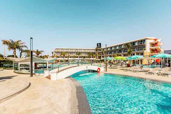 Billede af en pool med en lille bro og hotelbygning i baggrunden. (AI-genereret tekst)