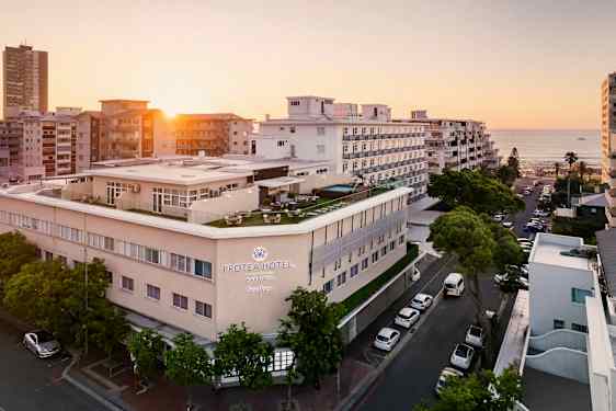 Hotelbygning ved havet omgivet af andre bygninger i solnedgang. (AI-genereret tekst)