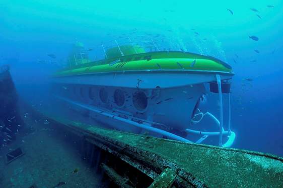 Undervandsudsigt af en ubåd ved siden af et gammelt skibsvrag omgivet af fisk. (AI-genereret tekst)