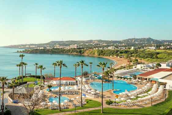 Udsigt over hotelområde med swimmingpools og udsigt til en bugt med blåt vand og grønne omgivelser. (AI-genereret tekst)