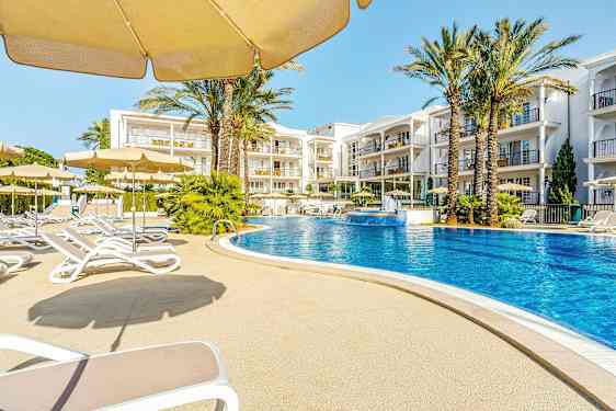 En udendørs pool omgivet af liggestole og parasoller med hotelbygninger i baggrunden. (AI-genereret tekst)