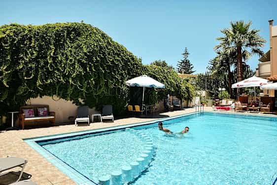 En udendørs pool omgivet af grønne områder og liggestole. (AI-genereret tekst)