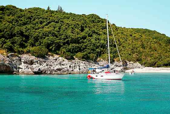 Sejlbåd på turkis vand nær en frodig kyst. (AI-genereret tekst)