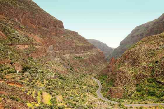 En smal vej snoer sig gennem en dal omgivet af stejle bjerge med grøn vegetation. (AI-genereret tekst)