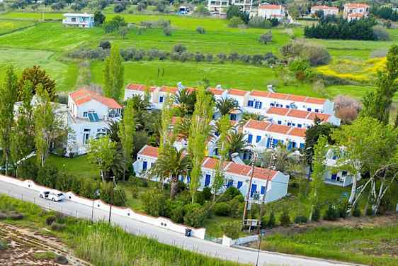 Luftfoto af hvide bygninger med røde tage omgivet af grønne områder og et landskab. (AI-genereret tekst)