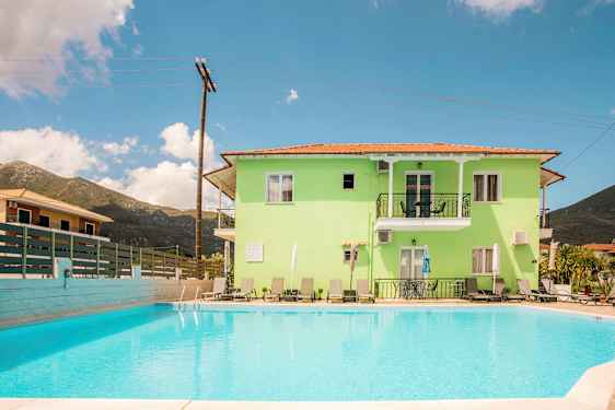 En lysegrøn bygning med altaner og solsenge, foran en udendørs swimmingpool. (AI-genereret tekst)