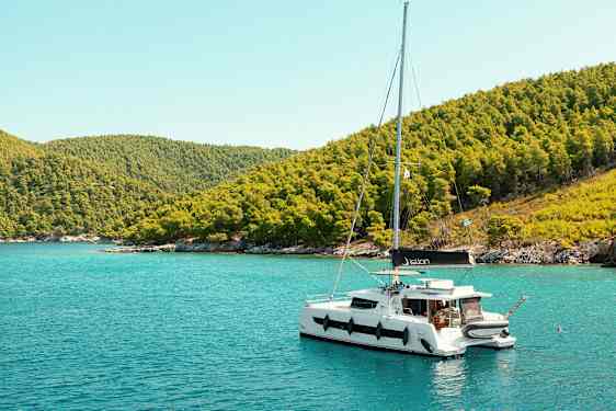 Sejlbåd fortøjet ved en kyst med frodige bakker. (AI-genereret tekst)