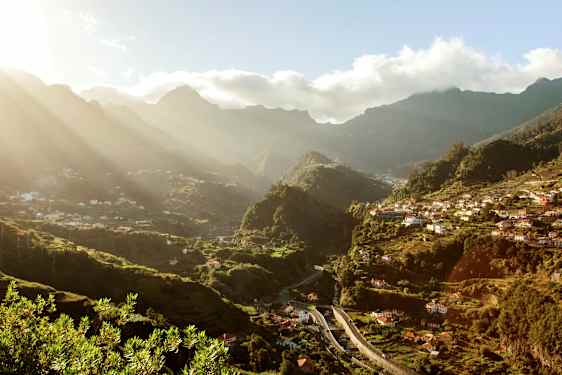 Udsigt over en grøn dal med huse og bjerge i baggrunden under en solrig dag. (AI-genereret tekst)
