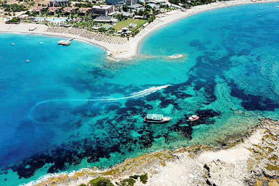 Luftfoto af en sandstrand ved et turistområde med klart blåt vand. (AI-genereret tekst)