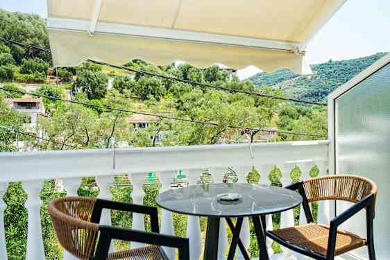 Udsigt fra en balkon med et lille rundt bord og to stole, omgivet af grønne områder og et bakket landskab. (AI-genereret tekst)