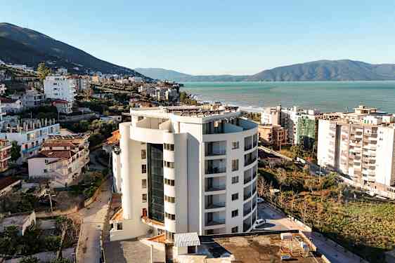 En høj bygning tæt på havet, omgivet af bygninger og grønt. (AI-genereret tekst)