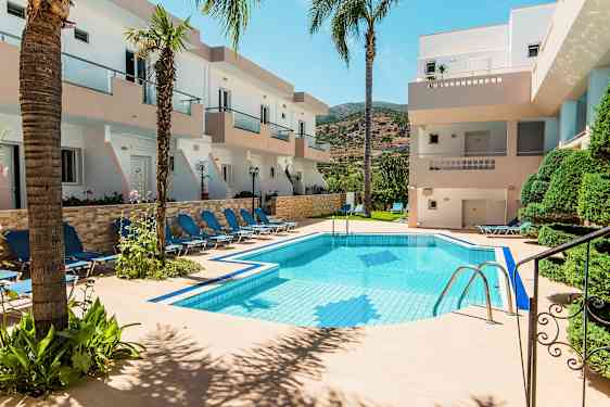 Billede af en pool omgivet af liggestole og bygninger med altaner. (AI-genereret tekst)