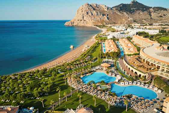 Luftfoto af et hotelområde med swimmingpools, grønne områder og en nærliggende strand ved havet. (AI-genereret tekst)