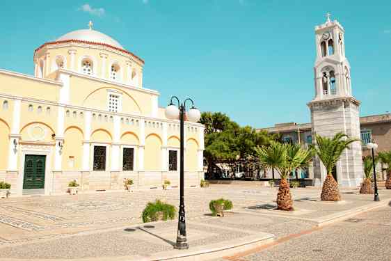 En gul bygning med kuppel og et klokketårn samt palmer og gadelys. (AI-genereret tekst)