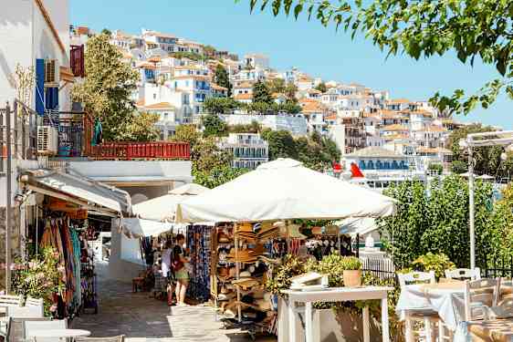 En malerisk by med hvide huse med røde tage på en skråning, parasoller og salgsboder i forgrunden. (AI-genereret tekst)