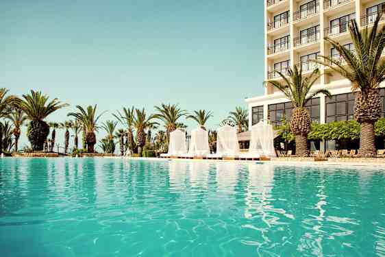 Udendørs pool med et hotel i baggrunden og omgivende palmetræer. (AI-genereret tekst)