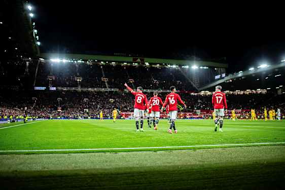 Fodboldspillere i røde trøjer på en oplyst fodboldarena under en aftenmatch. (AI-genereret tekst)