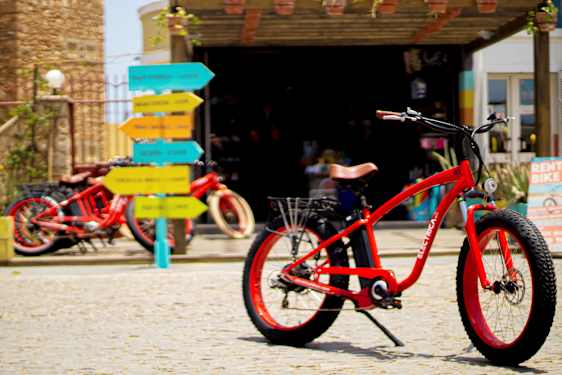 Rød cykel på brostensbelægning med farverige vejskilte i baggrunden. (AI-genereret tekst)