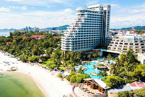 Billede af en kyst med en sandstrand, palmer og et stort hotelkompleks med poolområde. (AI-genereret tekst)