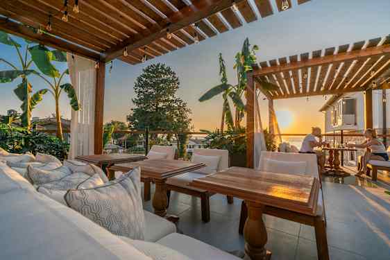 Udendørs område med træpergola, siddepladser og udsigt ved solnedgang. (AI-genereret tekst)