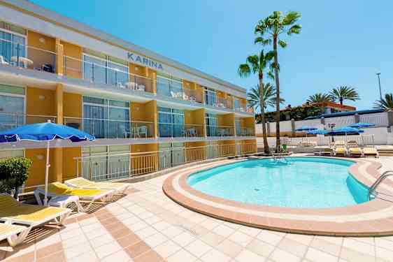 En udendørs pool med liggestole tæt på en lejlighedsbygning og palmer. (AI-genereret tekst)