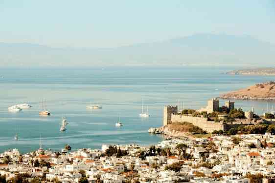 Billede af en by ved havet med en gammel borg nær kysten og både på vandet. (AI-genereret tekst)