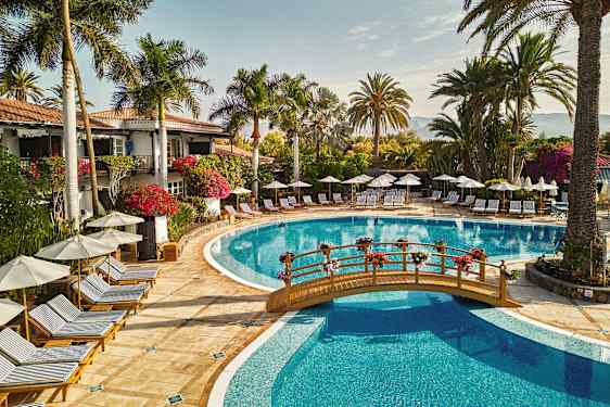 Udendørs poolområde med liggestole, parasoller og omkringliggende palmer. (AI-genereret tekst)