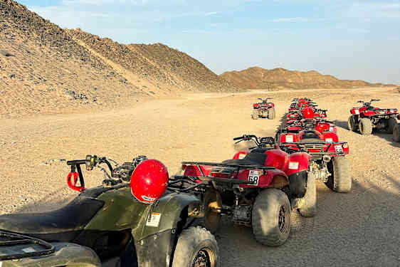 En række firehjulede ATV'er er parkeret på en ørkenvej omgivet af sandede bakker. (AI-genereret tekst)