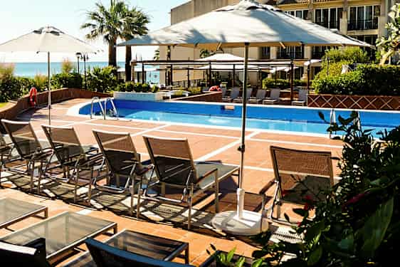 En udendørs pool med liggestole og parasoller. (AI-genereret tekst)