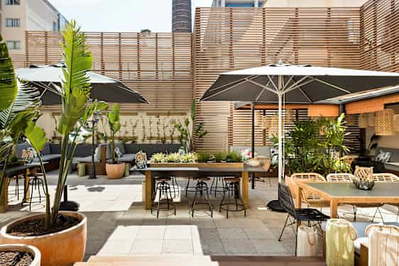 En udendørs terrasse med borde, stole og plantepynt, omgivet af træpaneler. (AI-genereret tekst)