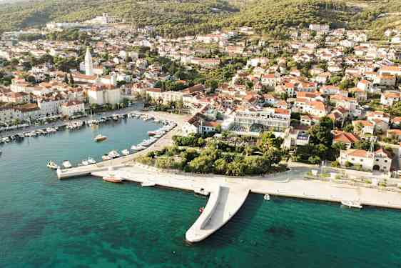 Luftfoto af en kystby med både i en havn og huse med røde tage. (AI-genereret tekst)