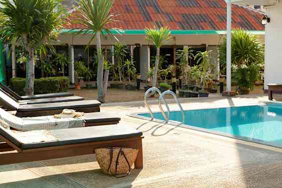 Liggestole ved en pool med grønne træer og bygning i baggrunden. (AI-genereret tekst)