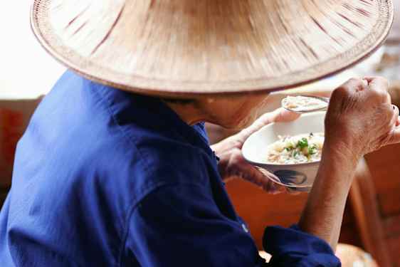 En person i blåt tøj og hat spiser fra en skål med en ske. (AI-genereret tekst)