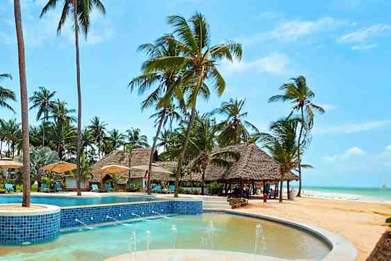 En pool med blå fliser omgivet af solsenge, parasoller og palmer ved stranden. (AI-genereret tekst)