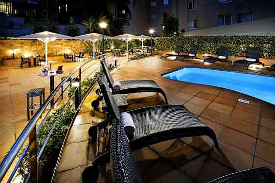 Hotellets poolområde med liggestole og parasoller ved et oplyst og flisebelagt udendørsområde. (AI-genereret tekst)