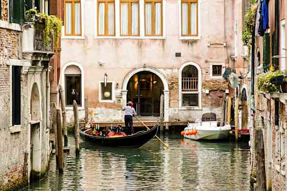 En gondol med en gondoliér flyder på en kanal foran en bygning. (AI-genereret tekst)