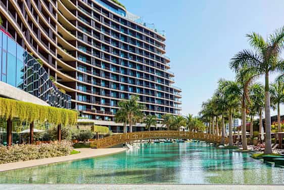 Billede af en moderne bygning med glasfacade ved en pool omgivet af palmer. (AI-genereret tekst)