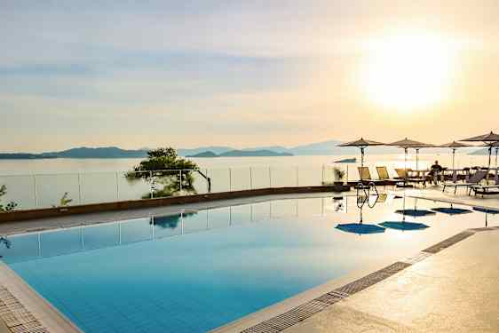 En swimmingpool med udsigt over havet og solnedgangen, parasoller og liggestole ved kanten. (AI-genereret tekst)