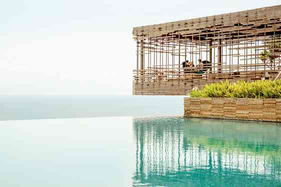 Udsigt over en infinitypool med havet i baggrunden og en træpavillon, der svæver ved kanten. (AI-genereret tekst)