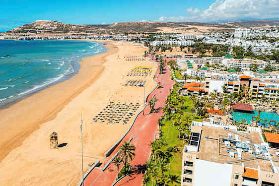 Strand med række af parasoller og havet i baggrunden. (AI-genereret tekst)