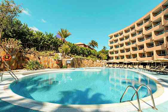 Billede af en pool med omkringliggende liggestole og en fler-etagers hotelbygning i baggrunden. (AI-genereret tekst)