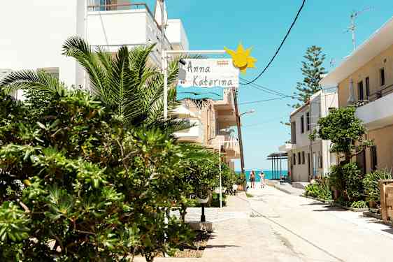 En solrig gade med grønne områder, bygninger og et skilt med teksten 'Anna Katerina'. (AI-genereret tekst)