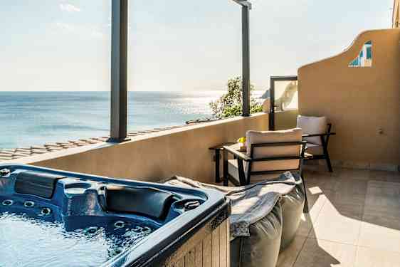 En terrasse med jacuzzi, siddepladser og udsigt over havet under en tagpergola. (AI-genereret tekst)
