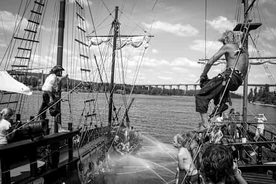 En scene på et gammeldags piratskib med personer, der interagerer og vandspredning mellem skibene. (AI-genereret tekst)